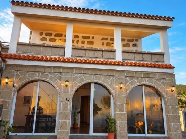 A two-story building with stone walls, a tiled roof, and large arched windows.