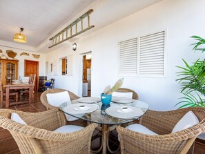 A dining area with wicker furniture, a glass table, and a blue vase with a cactus.