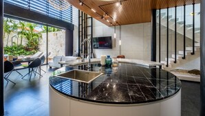 A modern kitchen with a black marble countertop, a built-in sink, and a large flat-screen TV mounted on the wall. - Alex Villas Complex N1 (Canggu)