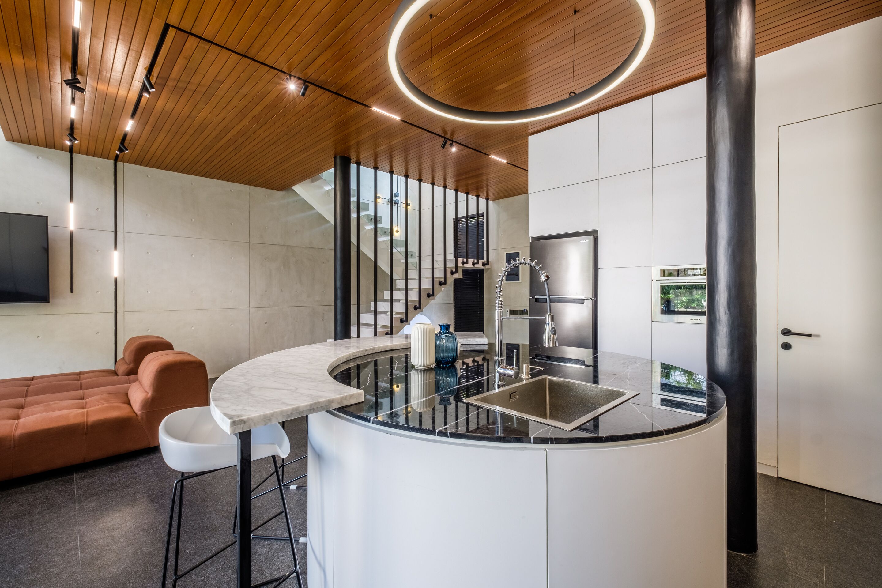 Een moderne keuken met een gebogen kookeiland, roestvrijstalen apparatuur en een houten plafond.