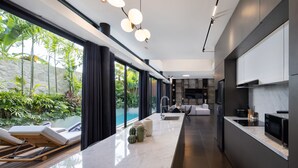 A modern kitchen with a marble countertop, built-in appliances, and a large window overlooking a pool and greenery. - Alex Villas Complex N1 (Canggu)