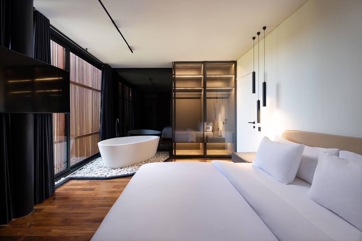A modern hotel room with a large bed, a bathtub, and a walk-in closet.