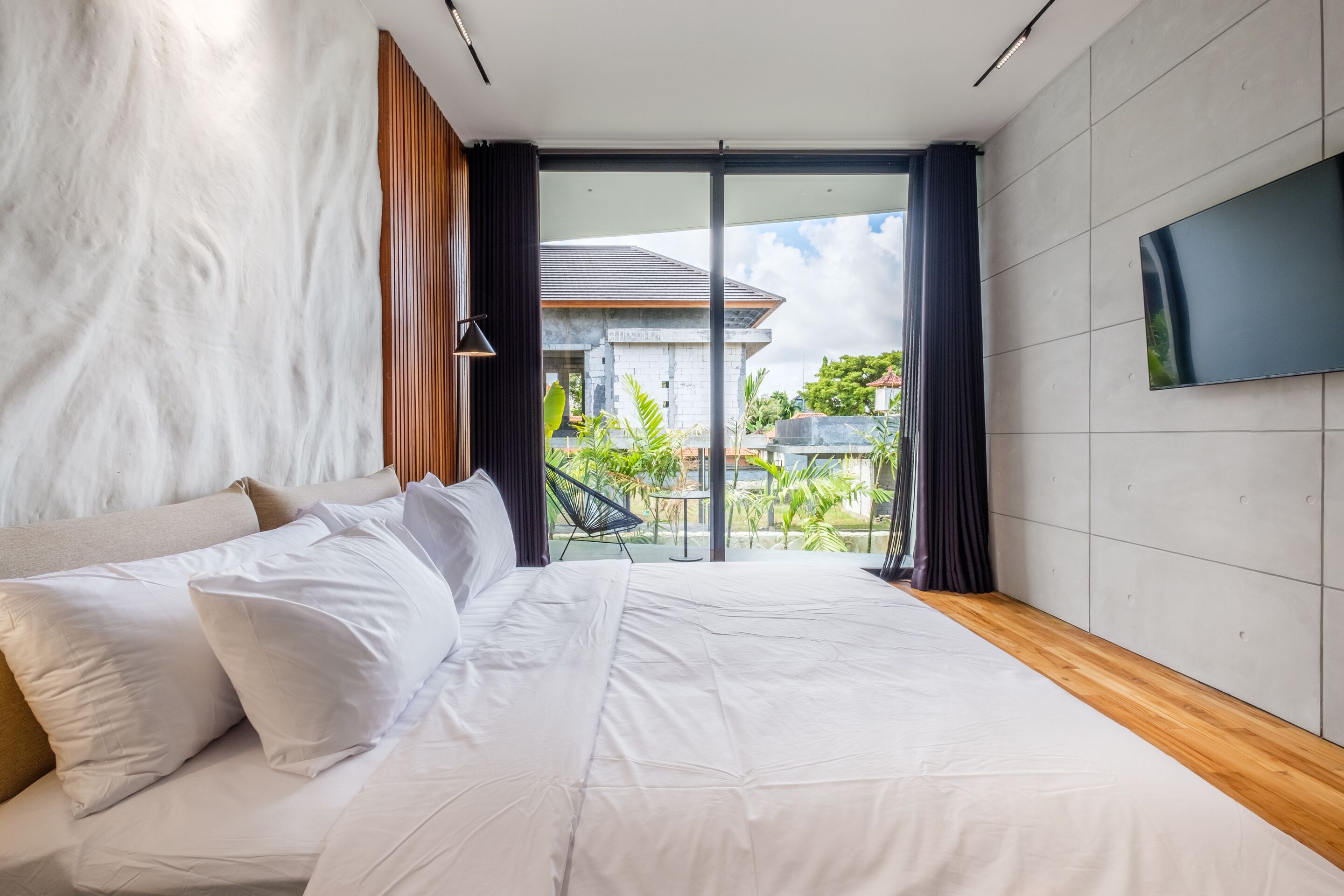 A modern bedroom with a large bed, a TV on the wall, and a view of the outside.