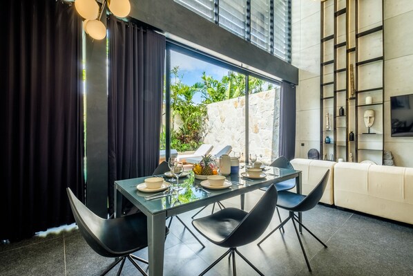 A modern dining area with a glass table, black chairs, and a view of the outdoors.
