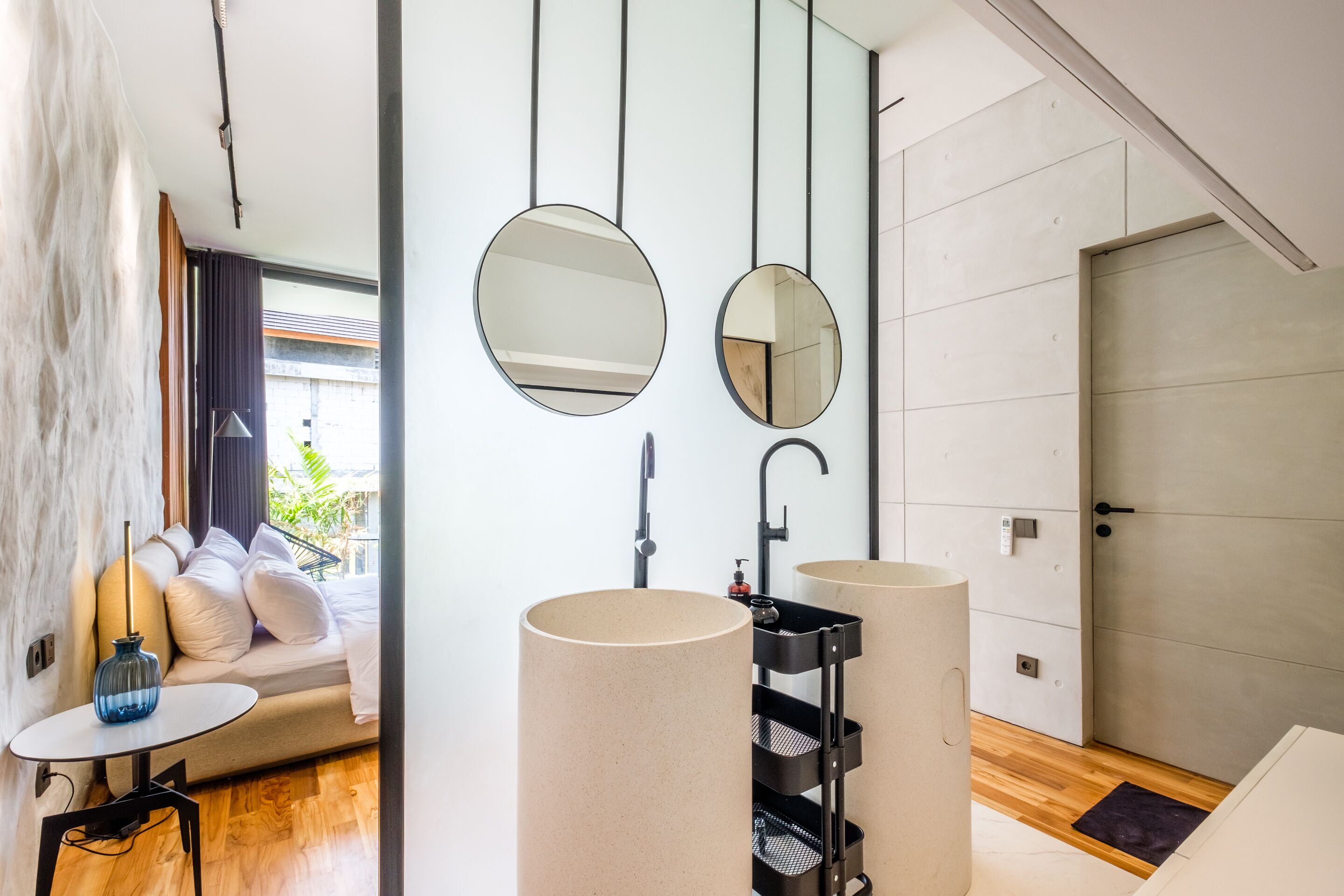 A modern bathroom with two round mirrors, a black sink, and a wooden floor.