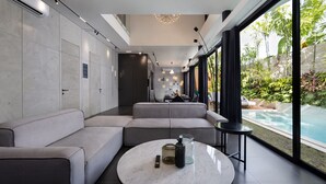 A modern living room with a sectional sofa, a round coffee table, and a view of a swimming pool. - Alex Villas Complex N1 (Canggu)