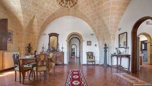 A spacious room with a high arched ceiling, a central table with chairs, a patterned rug, and a mirror on the wall. - 2040 Antica Masseria Casa Rossa - Appartamento Frantoiana by Barbarhouse (Oria)