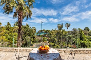 A table with a fruit basket and a metal chair in a garden setting with a view of trees and a fence. - 2349 Villa Mina by Barbarhouse (Melendugno)