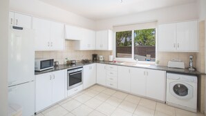 Une cuisine moderne avec des meubles blancs, un four à micro-ondes, un four traditionnel et un lave-linge.