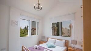 Une chambre à coucher avec un lit, deux tables de chevet, un lustre et de grandes fenêtres.
