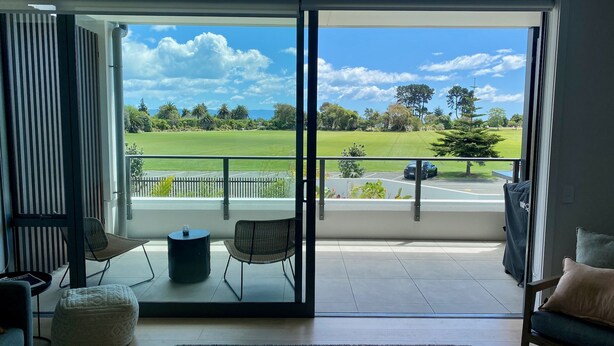 A balcony with a view of a golf course, a car, and a fence. - Tahuna Beach Apartment - Easy walk to the beach & lots of local eateries! (Nelson)