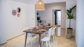 A dining area with a long table, white chairs, and a hanging light fixture.