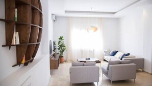 A modern living room with a grey sofa set, a wooden bookshelf, and a potted plant.