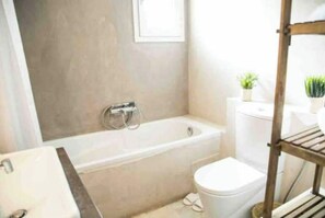 Bathroom features a bathtub, toilet, and sink, with a potted plant on the wall.