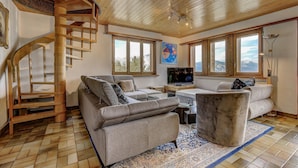 A spacious living room with a wooden spiral staircase, a large sofa, a coffee table, and a television.