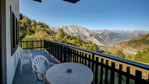 A balcony with a table and chairs, offering a view of mountains.