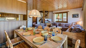 A wooden dining table set with plates, glasses, and cutlery. There is a staircase leading to an upper level, a sofa, and a bed with plaid bedding.