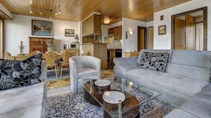 A modern living room with a wooden ceiling, a grey sofa, a white armchair, and a glass coffee table.