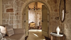 A stone-walled hallway with a wooden door, a wooden chair, a small table, and a white sculpture. - 3 Bedroom Villa with private swimming pool (Zakynthos)