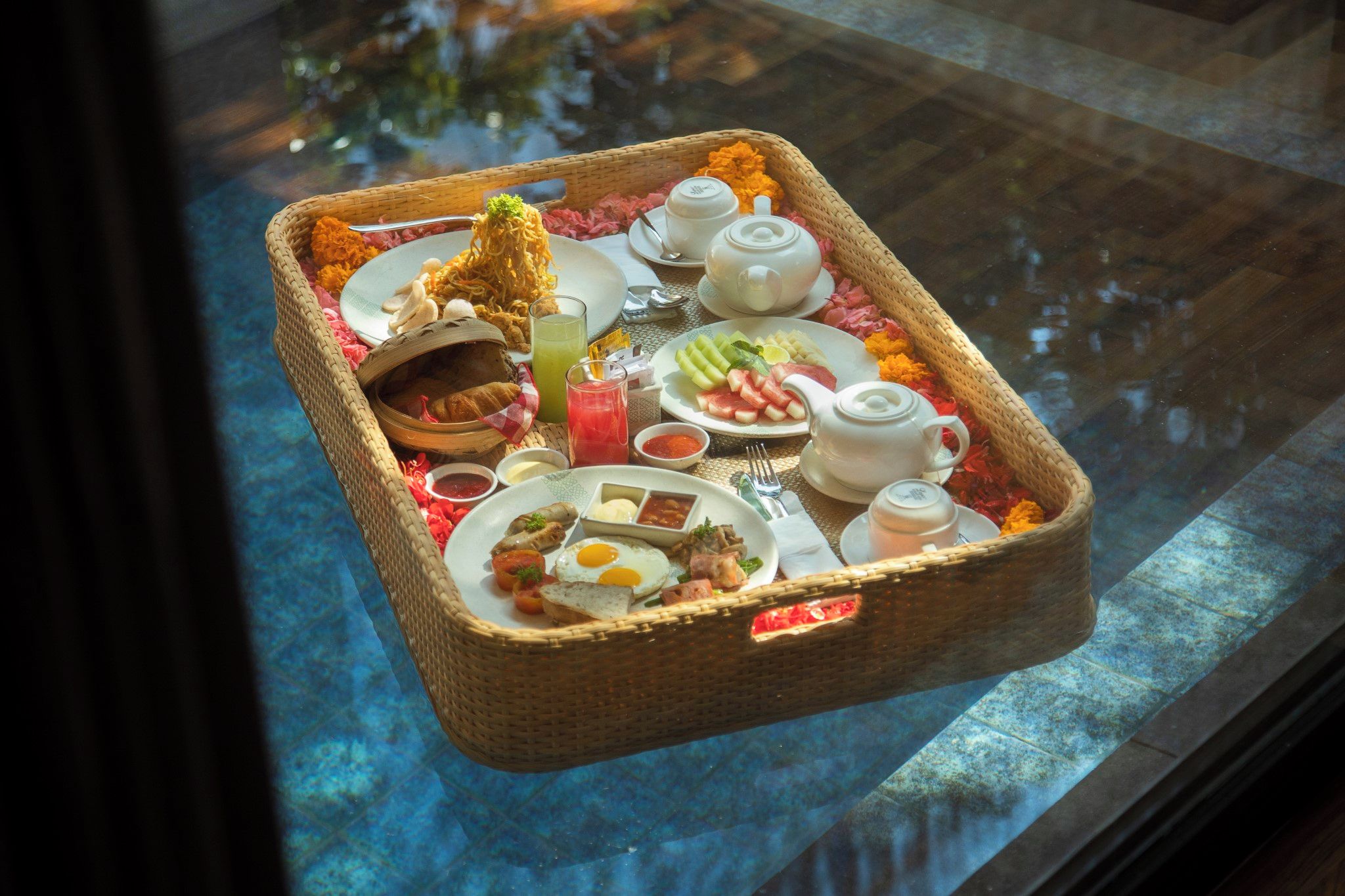 A breakfast tray with various food items, a teapot, and a cup on a table by a window.