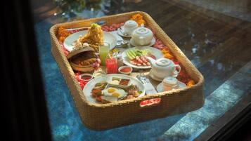 A breakfast tray with various food items, a teapot, and a cup on a table by a window.