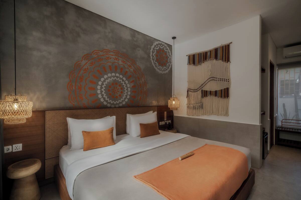 Una habitación de hotel moderna con una cama grande, un cabecero con diseño tejido, una pared con motivos decorativos y una pieza de macramé colgante.