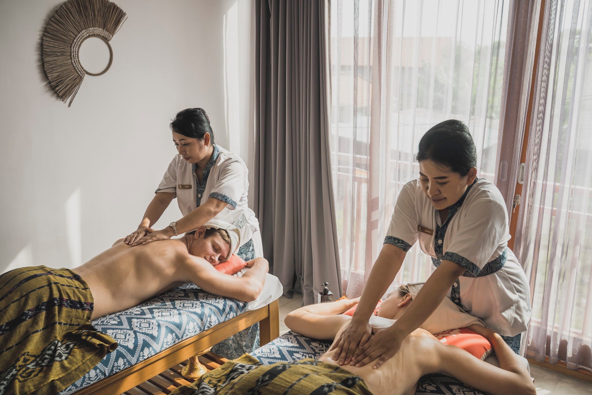 A massage therapy session in a room with a bed, a window with curtains, and a wall decoration.