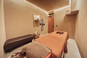 Una habitación de hotel con cama, una banca, un espejo, una bata y una mesita de noche con artículos de aseo.