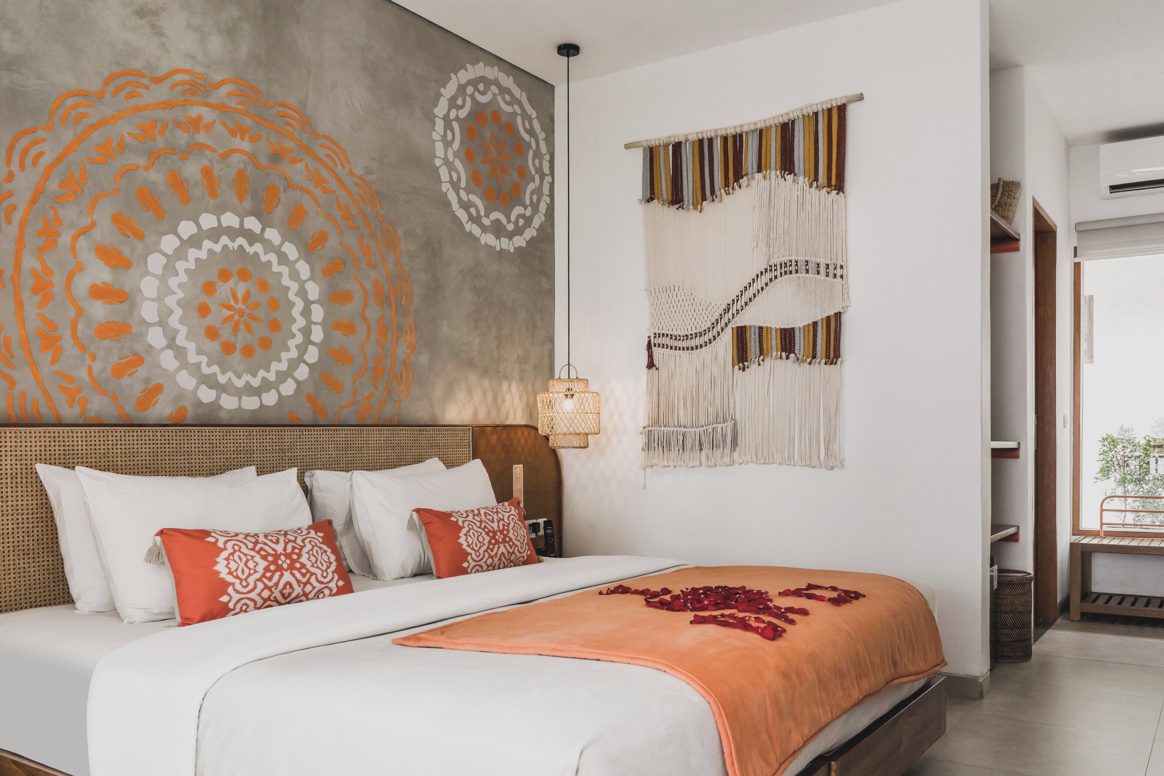 A bed with white and orange bedding, a wall with a circular design, and a macrame wall hanging.