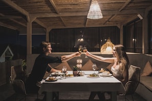 A couple toasting at a table with a candlelight centerpiece, surrounded by wicker chairs and a wooden ceiling. - Roomates Beach Hostel Canggu by Ini Vie Hospitality (Canggu)