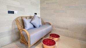 Un canapé en osier avec des coussins bleu clair, placé contre un mur dont le motif présente une texture et des couleurs claires.