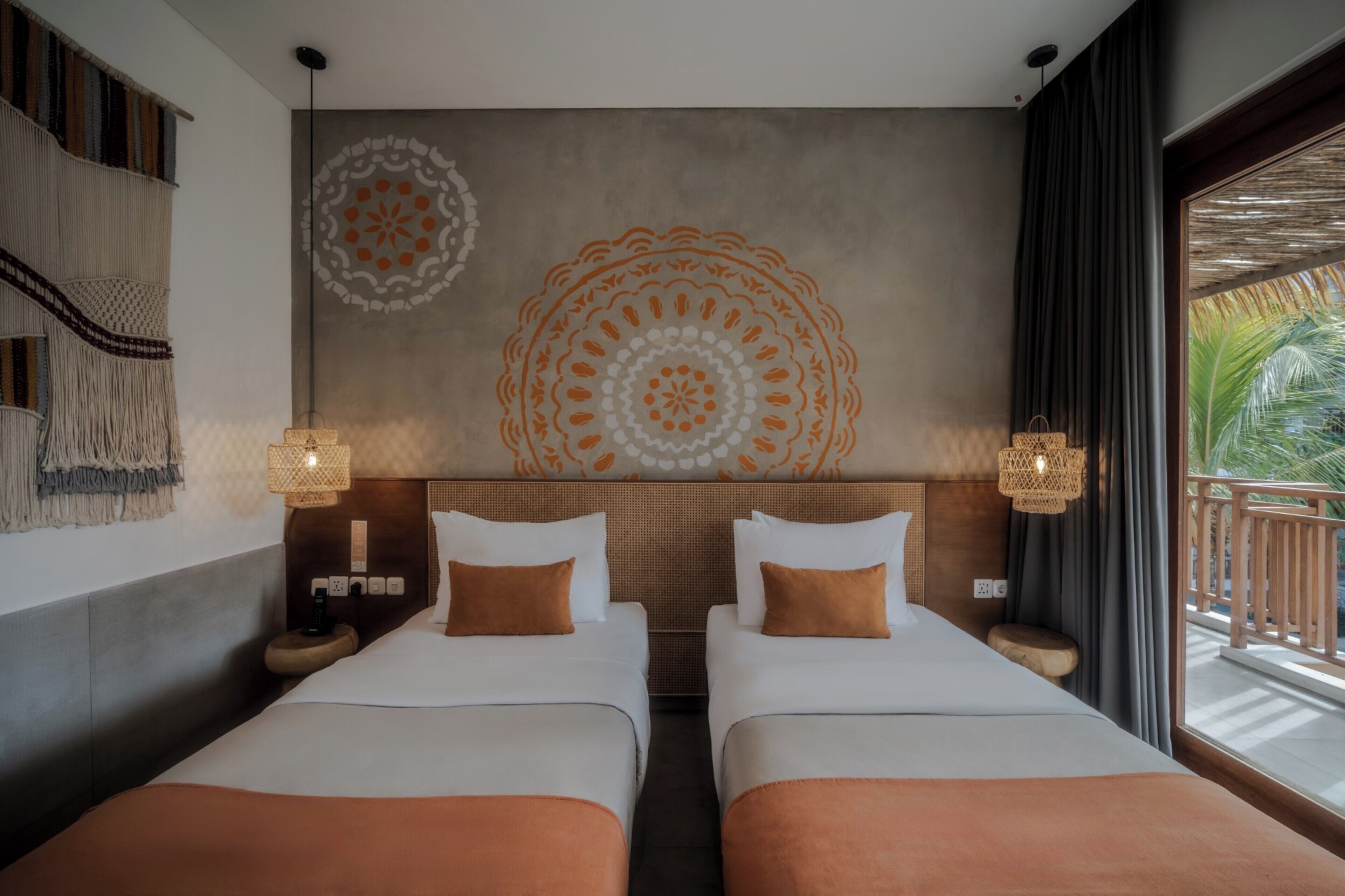 Habitación de hotel con dos camas, un mural grande en la pared, un balcón con vistas y un tapiz tejido.