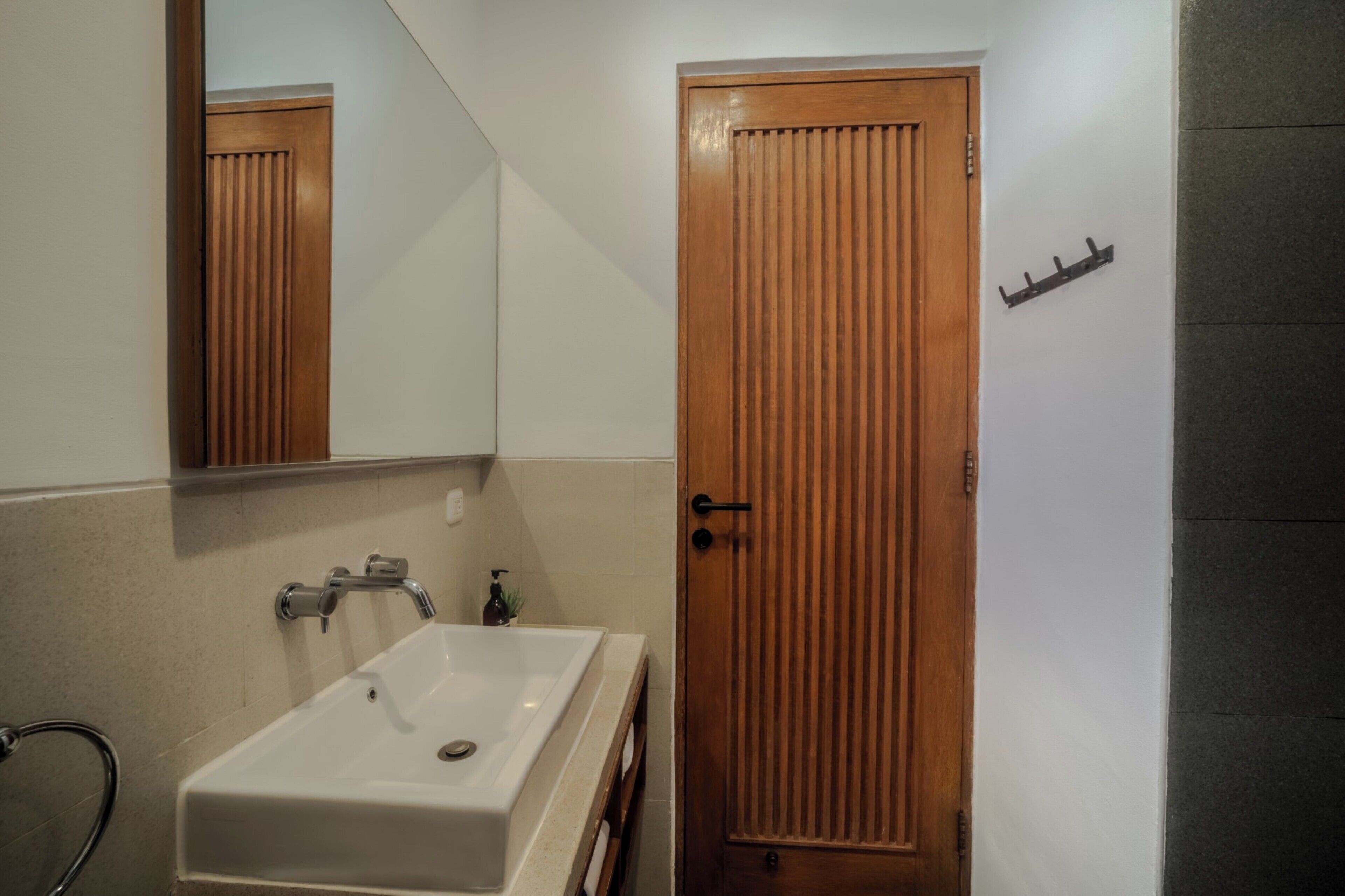 Ein Badezimmer mit Waschbecken, Holztür, Spiegel und Handtuchhalter.