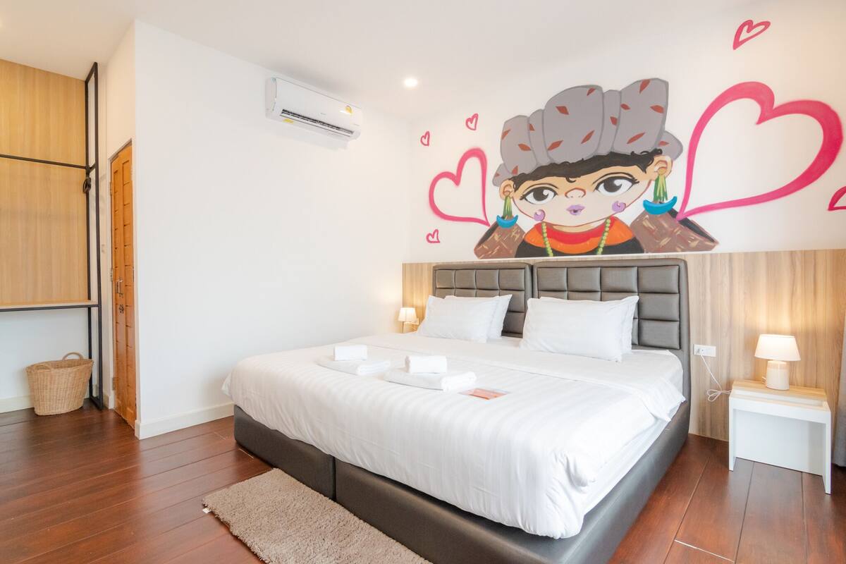 Ein Schlafzimmer mit einem großen Bett, einem an der Wand gemalten Wandbild an der Kopfteil, einem Nachttisch mit Lampe und einem Holzschrank.