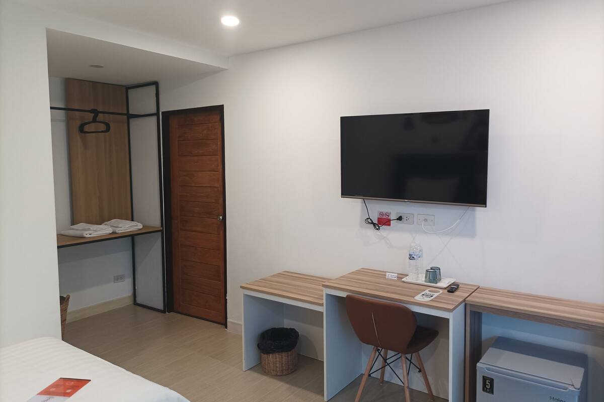 Ein Hotelzimmer mit einem Bett, einem Schreibtisch mit Stuhl, einem an der Wand befestigten Fernseher, einem kleinen Kühlschrank und einem Holzschrank.