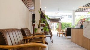 Un espace d’accueil avec un comptoir de réception en bois, un coin salon avec des fauteuils en cuir et une vue sur l’extérieur.