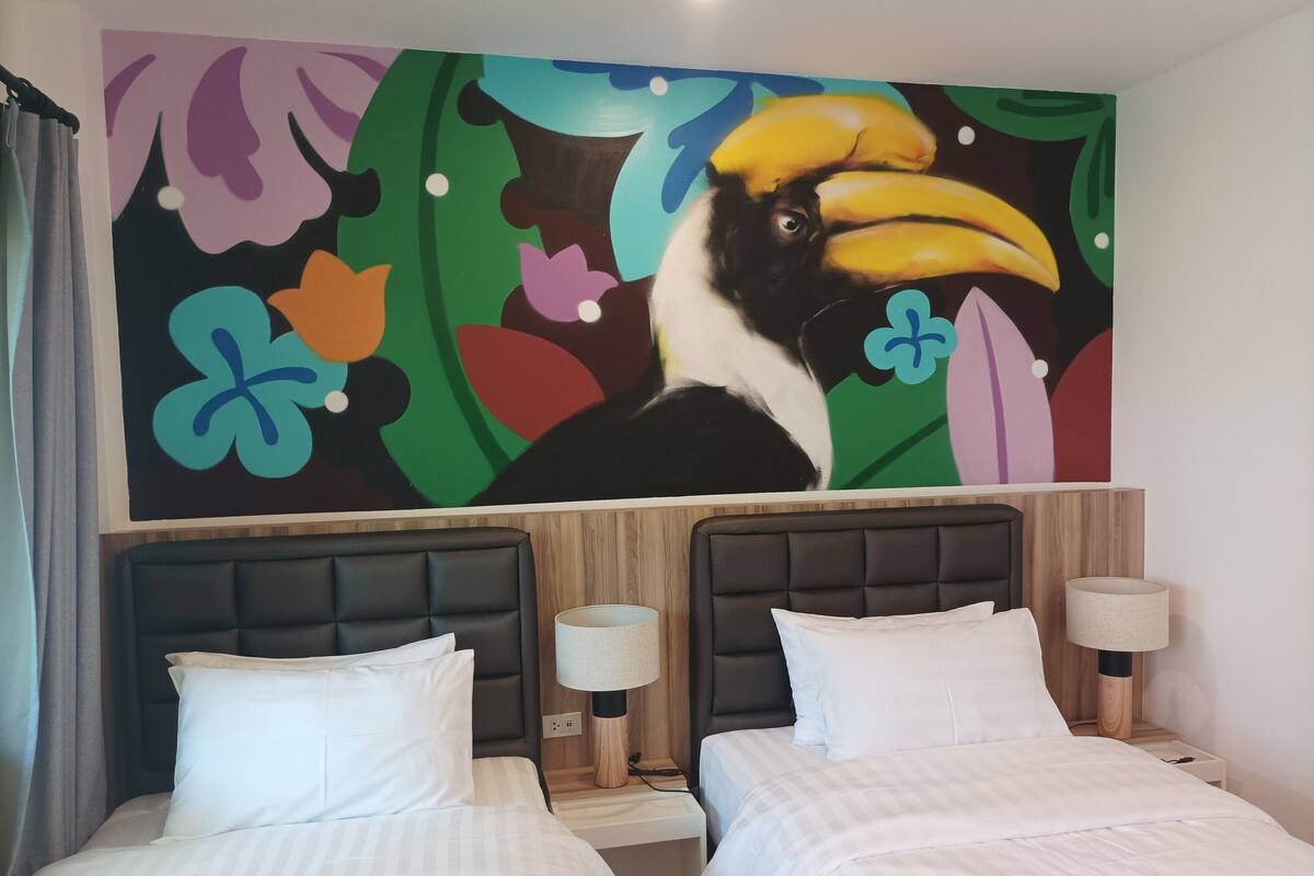 Ein Hotelzimmer mit zwei Betten, einem großen Wandbild mit einem Tukan und einem hölzernen Kopfteil.