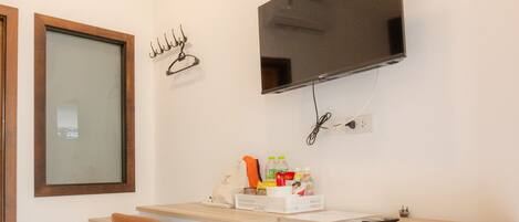 Habitación de hotel compacta con cama, escritorio y silla, un refrigerador pequeño, televisión montada en la pared y ventana con marco de madera.