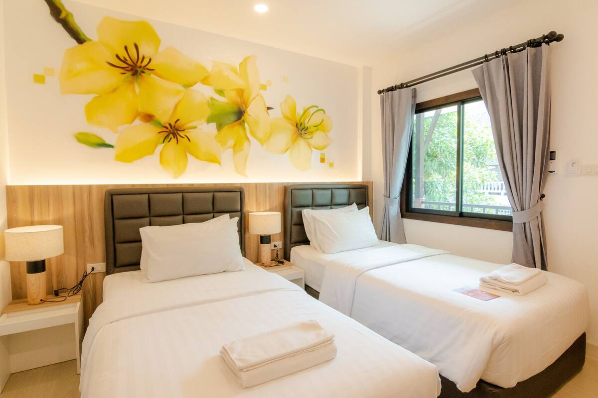Ein Hotelzimmer mit zwei Betten, einer großen Blumenwand, einem Fenster mit Vorhängen und einer Nachttischlampe.