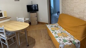 Un espacio habitable compacto con una mesa de comedor de madera, un sofá con un cojín floral, un televisor y un mueble pequeño.