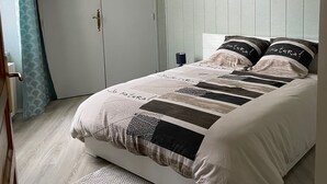Un dormitorio con cama, una puerta, un cuadro en la pared y una lámpara en el techo.