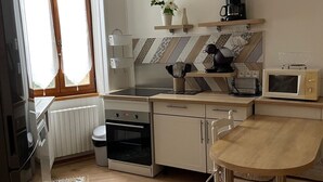 Cocina moderna con armarios blancos, encimera de madera, horno empotrado, microondas y lámpara colgante.