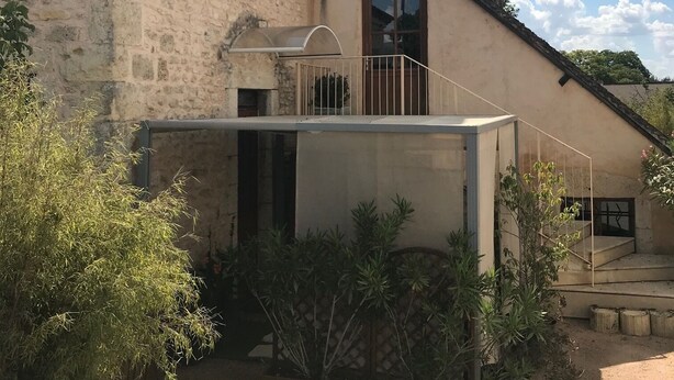 Un edificio con fachada de piedra, una extensión moderna con cerramiento de vidrio y una escalera que sube a un segundo piso.