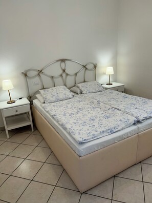 Een bed met een bloemenprintdeken, twee nachtkastjes met lampen en een effen muur.