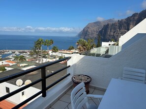 Un balcon avec vue sur la mer et les montagnes, une table blanche et une chaise.