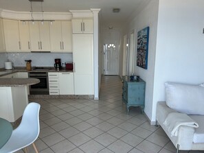 Eine Küche mit weißen Schränken, ein Essbereich mit Tisch und Stühlen sowie ein Wohnzimmer mit einer Couch und einem Bild an der Wand.