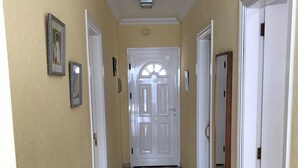 Un pasillo con una puerta blanca al final, un tapete pequeño en el suelo y dos cuadros en la pared.