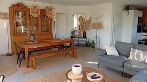 A living room with a wooden dining table, a grey sofa, and a coffee table with a remote control. - 3 bedroom house on the edge of a forest (Salles)
