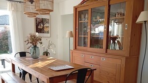 A dining area with a wooden table, benches, a black chair, a woven rug, a cabinet with glass doors, and hanging wicker lamps. - 3 bedroom house on the edge of a forest (Salles)