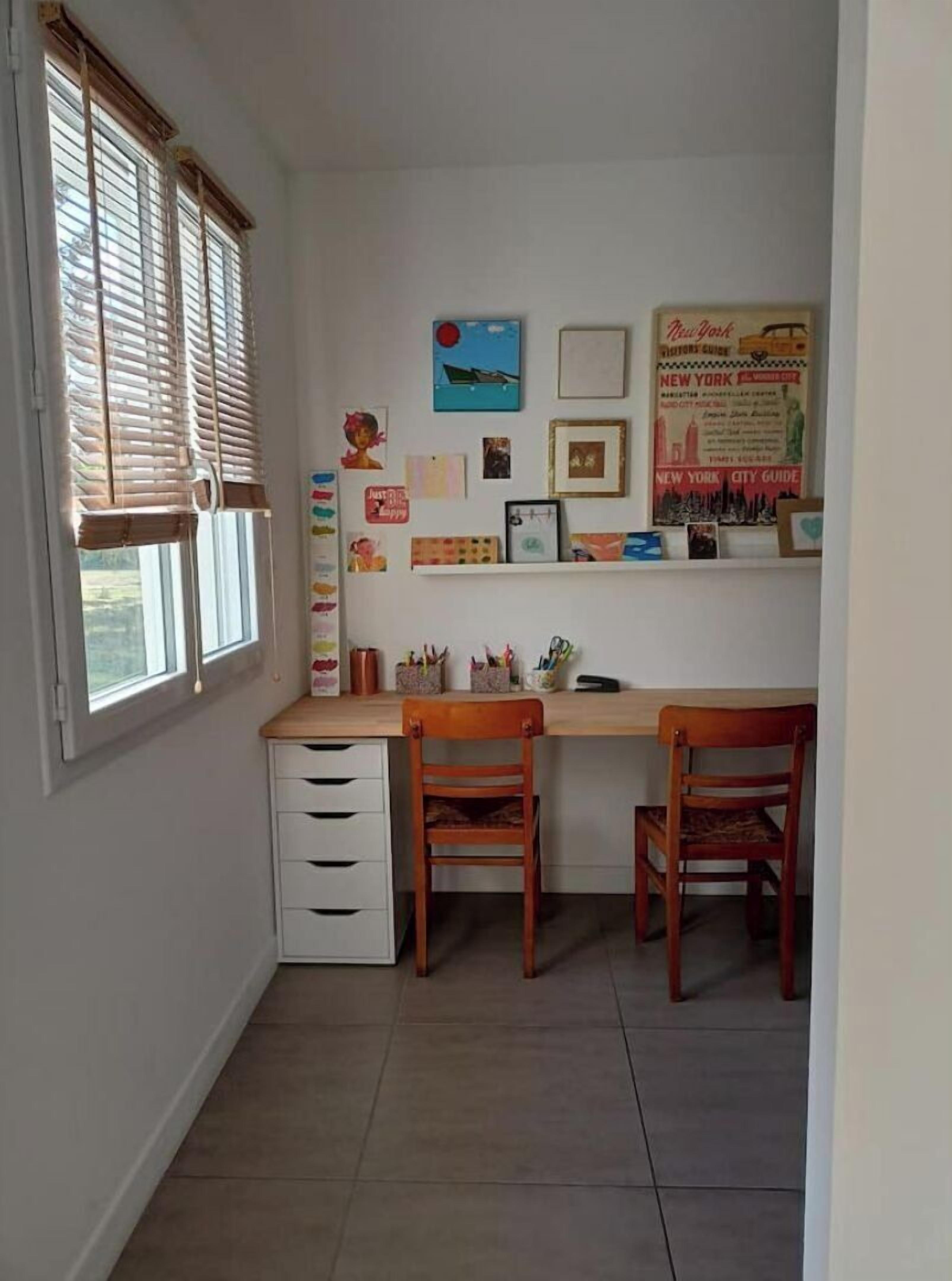 Een studeerkamer met een bureau, twee stoelen, een boekenkast en een raam met jaloezieën.